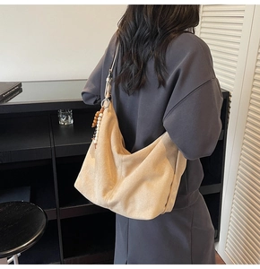Detail view of beige suede hobo bag with wooden bead tassel and adjustable shoulder strap