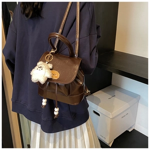 Detailed side view of dark brown faux leather backpack with plush bear charm accessory