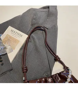 Détail du sac à bandoulière en cuir plissé marron avec une chaîne décorative en perles