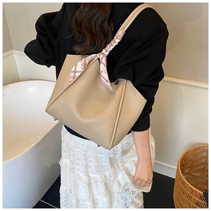 Dettaglio borsa tote beige con piedini in metallo e foulard di seta rosa sul manico