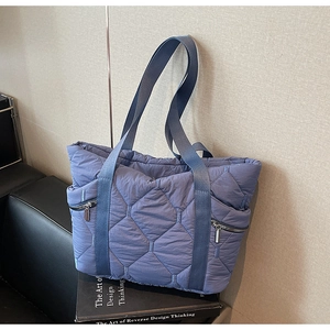 Detailed view of the blue quilted tote bag showing diamond stitching and metal zippers