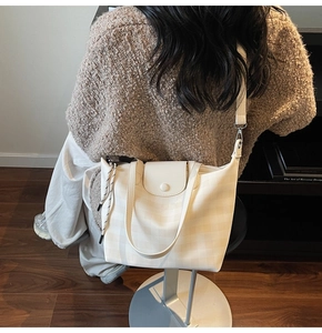 Detail of checkered tote bag with leather flap and strap in modern indoor setting