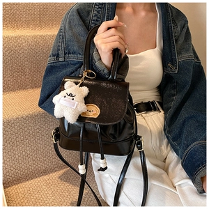 Close-up of black glossy patent leather bucket backpack with a cute plush bear charm