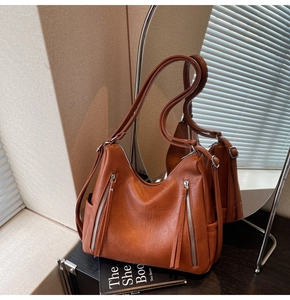 Detail view of brown leather Hobo bag featuring dual vertical zippers and long tassels