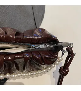 Détail du sac plissé en cuir verni marron foncé avec fermeture éclair et chaîne de perles