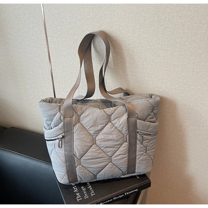 Detail of grey quilted tote bag featuring silver zippers and brown textile handles