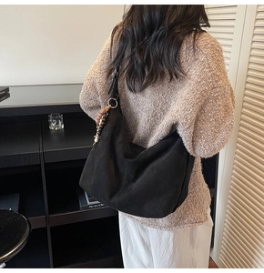 Detail of black suede hobo bag featuring decorative beaded tassel and matte leather texture