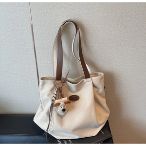 Detail of canvas tote bag featuring brown leather straps and a plush puppy charm accessory