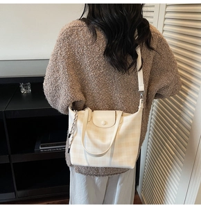 Detail of a beige checkered tote bag showing the texture, handle, and leather finish