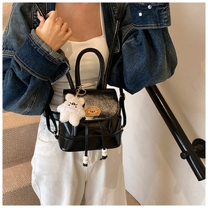 Detail of a shiny black mini backpack with a plush bear charm and drawstring closure