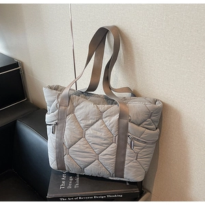 Detail of grey quilted tote bag featuring a functional metal side zipper and woven strap