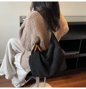 Detail view of black faux suede hobo bag with vintage beaded charm on a knit cardigan model