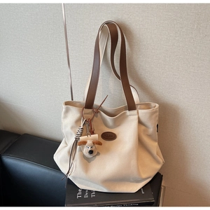 Close-up of canvas tote bag featuring brown leather handles and a cute puppy plush charm