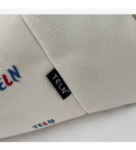Detailansicht der cremefarbenen Segeltuchtasche mit Stickerei und gewebtem Logo Etikett