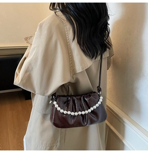 Detailed view of dark reddish-brown ruched glossy bag with elegant pearl chain accessory