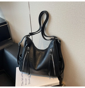 Detail of black leather hobo bag featuring dual silver zippers and long tassel pulls