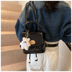 Detail of black patent leather bucket backpack with plush bear charm and drawstring