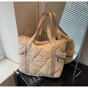 Detail of beige quilted tote bag showing diamond stitching and silver zipper pocket