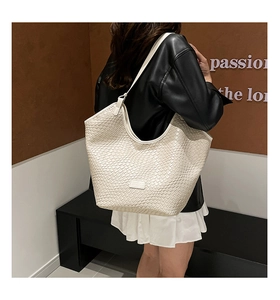 Detail of a large cream woven tote bag showing texture and size on a female model