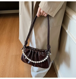 Detail of dark brown pleated handbag with glossy finish and large pearl chain decoration