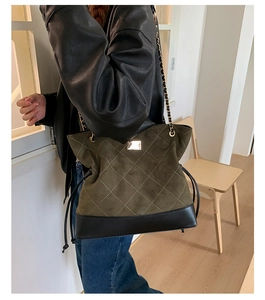 Detail of olive suede tote bag with beige quilted stitching and gold logo plate