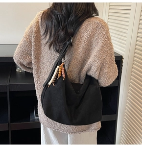 Detail of a black suede hobo bag with a decorative beaded tassel and metal ring strap