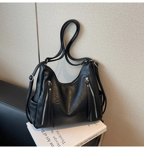 Detailed view of black leather hobo bag with silver zippers and side pockets on a book