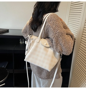 Close-up of checkerboard tote bag with adjustable leather strap and woven charm detail