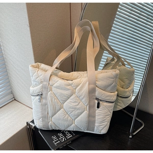 Detailed close-up of a white quilted puffer tote bag with zippers on a sleek shelf