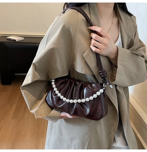 Detail of dark burgundy pleated handbag with pearl handle and long leather strap worn over a coat