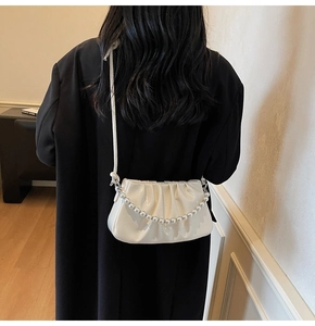 Detail of white pleated cloud bag with glossy finish and elegant pearl strap on black suit