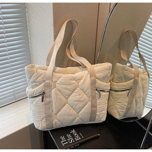 Detail of white quilted tote bag featuring large diamond stitching and silver zipper pockets