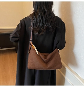 Détail du sac à bandoulière en daim marron avec pompon en bois sur manteau noir