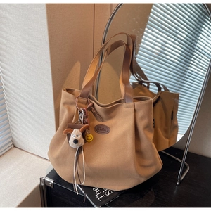 Detail of khaki canvas tote bag with brown handles and cute plush dog keychain