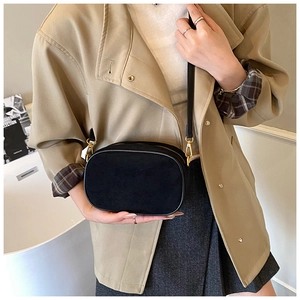 Detail of black frosted oval crossbody bag with gold hardware shown on shoulder