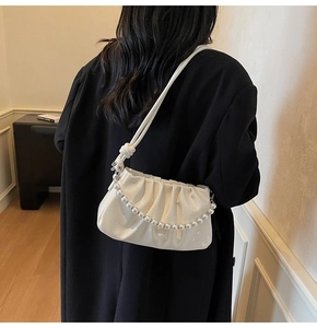 Detail of off-white pleated underarm bag with pearl chain strap worn on black coat