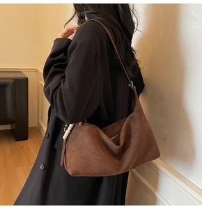Détail d'un sac cabas en daim marron avec breloque en perles blanches sur la bandoulière