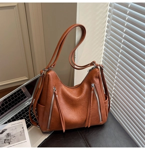 Detail view of caramel leather tote bag featuring dual vertical zippers and long tassels