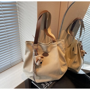 Detail of off-white canvas tote bag with brown leather straps and cartoon dog keychain