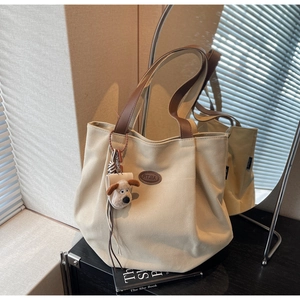 Detail of off-white canvas tote bag with brown leather handles and dog plush pendant