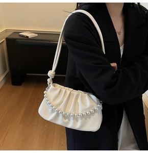 Detail of white pleated underarm bag with glossy texture and decorative pearl chain strap