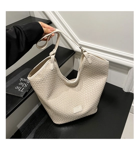 Detail of beige woven texture tote bag with leather logo patch in lifestyle setting