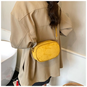 Detail view of a yellow suede-style crossbody bag with a slim strap and gold metal hooks