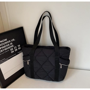 Detailed side view of black quilted tote bag with silver zipper pockets and padded straps