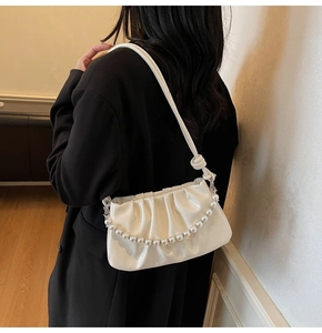 Detail of white pleated shoulder bag with pearl chain accessory on a black blazer