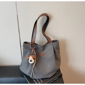 Detail of dark grey canvas tote bag with brown leather straps and plush puppy charm
