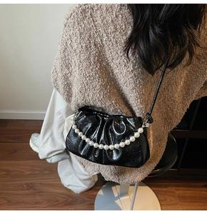 Detailed view of black pleated dumpling bag featuring glossy leather and large pearl chain