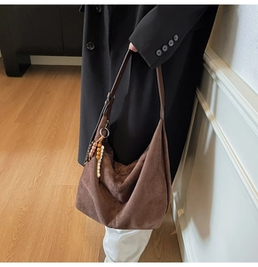 Detail of dark brown suede hobo bag with ethnic beaded charm and leather strap