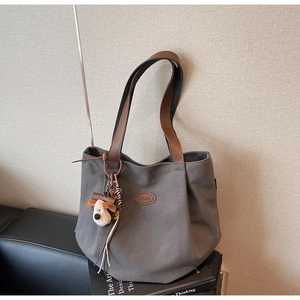 Detail of grey canvas tote bag with brown leather straps and a cute dog plush charm