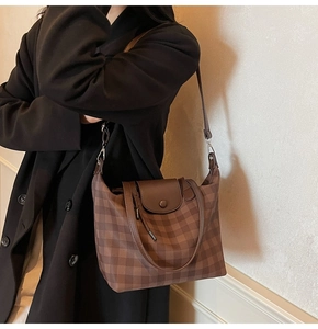 Detail of coffee plaid tote bag with brown leather flap on a black wool coat